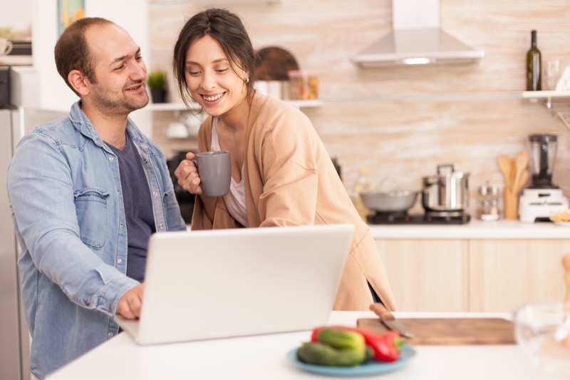 Una pareja revisa sus cuentas en la mesa de la cocina, con la computadora abierta y una taza de café